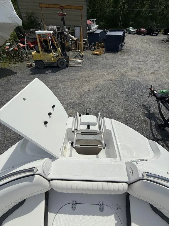 Slide: The Image of 2025 Stingray 231DC boat with open storage compartment and ladder, parked in a gravel lot. - 35