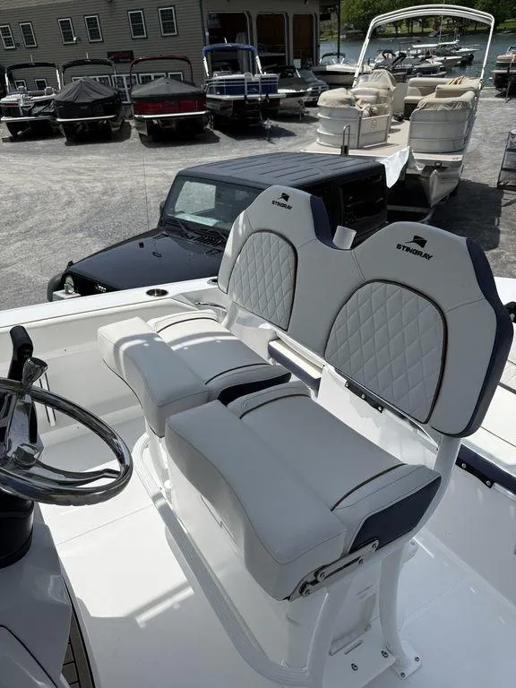 Slide: The Image of 2025 Stingray 216CC boat with dual cushioned seats and steering wheel, parked in a marina. - 11