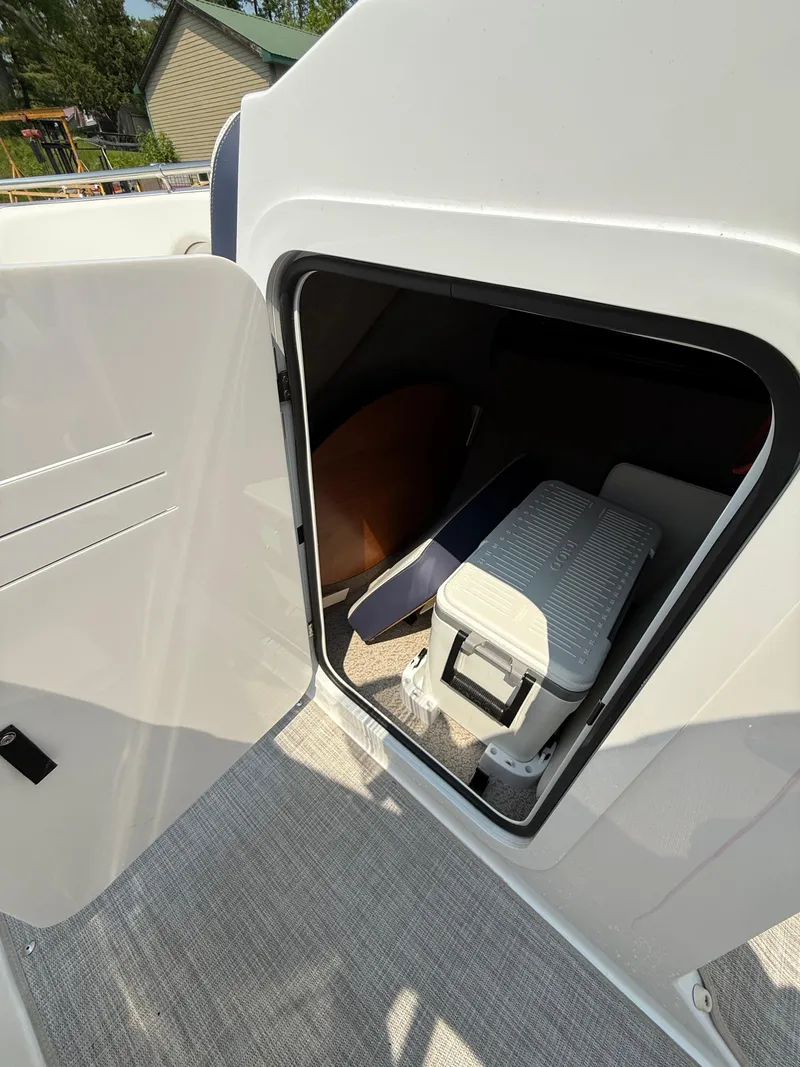 Slide: The Image of 2025 Stingray 211DC boat interior storage compartment with open door, showcasing seating and storage space. - 23