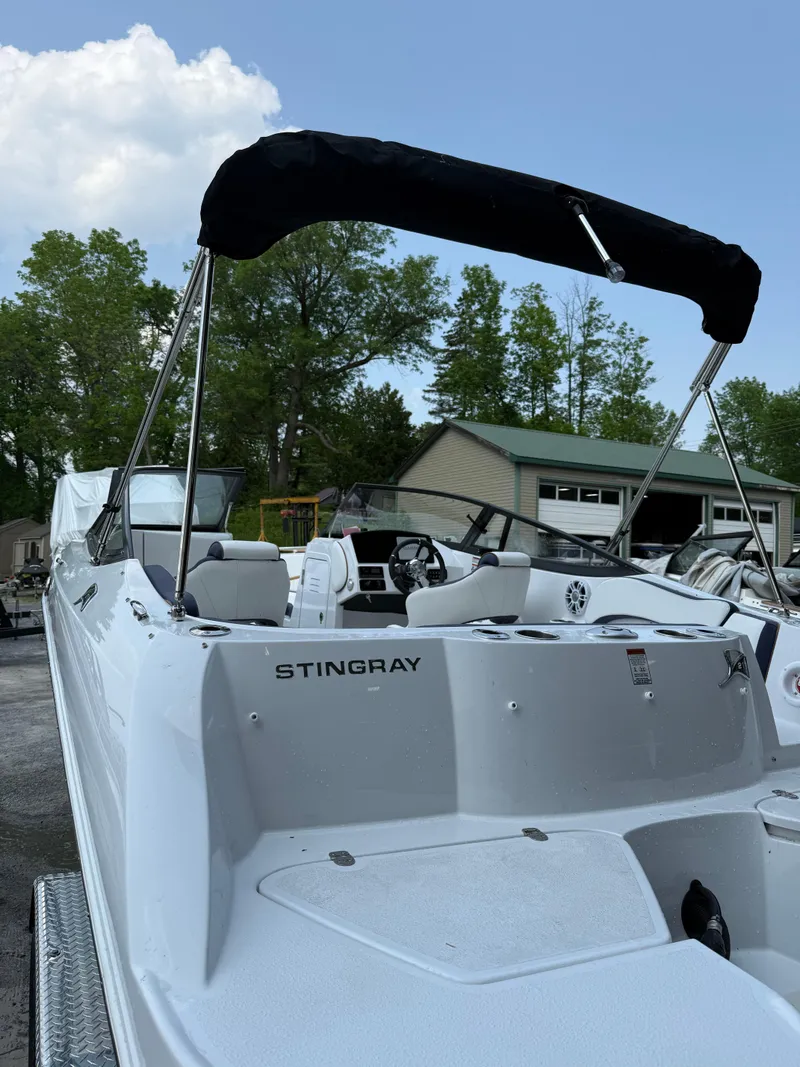 Slide: The Image of 2025 Stingray 211DC boat with canopy, parked outdoors near trees and buildings. - 4