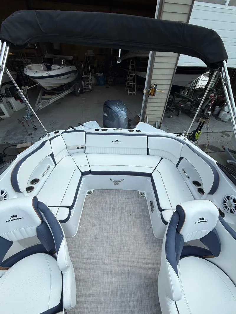 Slide: The Image of 2025 Stingray 211DC boat interior with white seating and canopy in a garage setting. - 9
