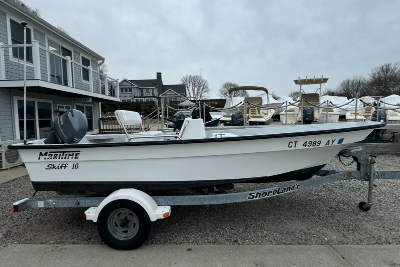 Slide: The Image of 2003 Maritime 1690 Skiff 16 boat on trailer, parked near waterfront buildings. - 0