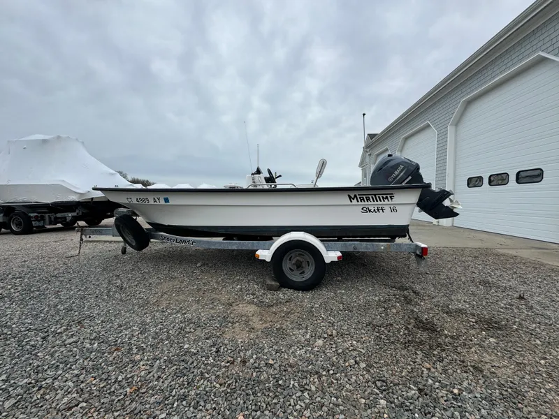 Slide: The Image of 2003 Maritime 1690 Skiff 16 boat on trailer, parked near a large building. - 1