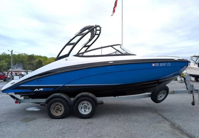 Slide: The Image of 2017 Yamaha AR210 boat on trailer, blue and white design, parked outdoors. - 6