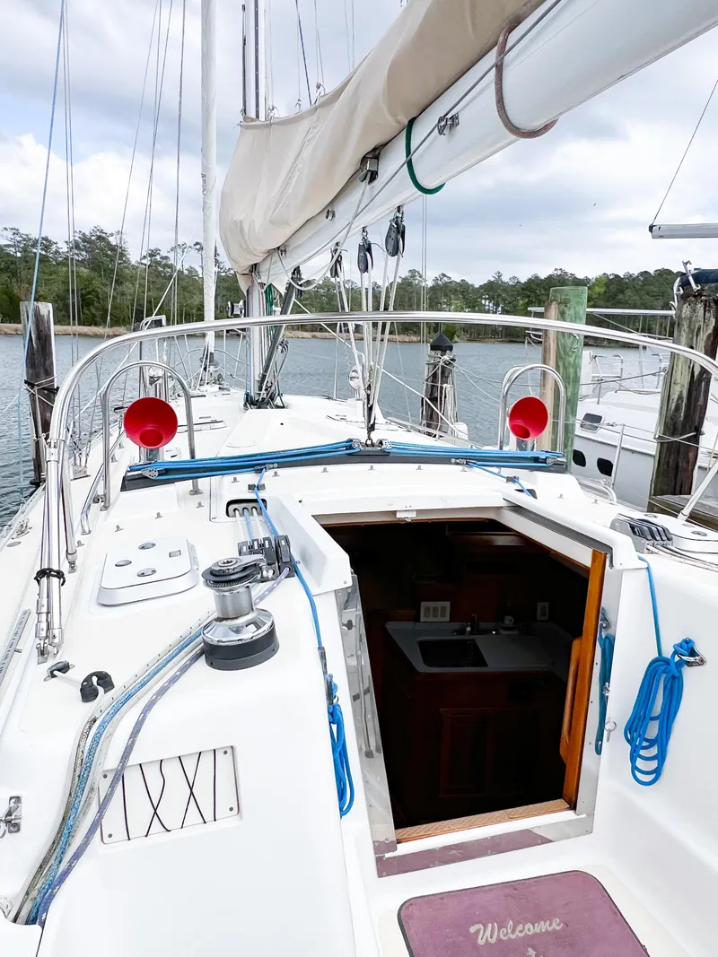 Slide: The Image of 1998 Saga 43 sailboat deck with open cabin entrance, docked by a serene waterfront. - 24