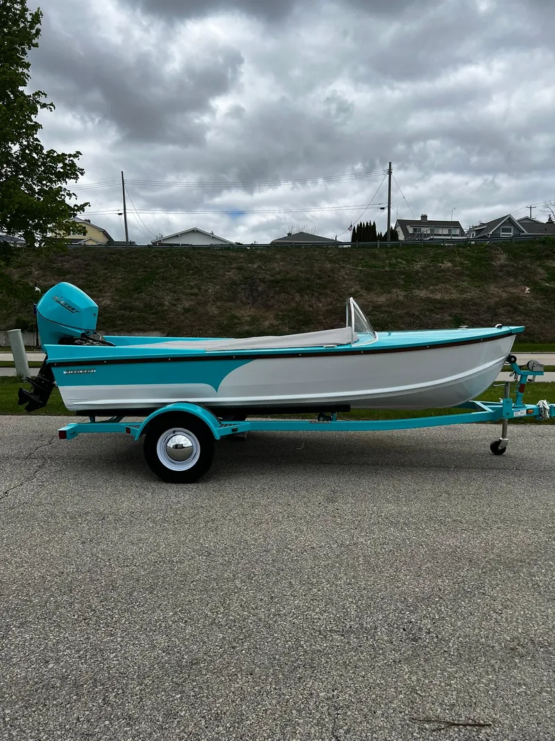 The Image of 2025 Starcraft 57 SKI CHAMP boat, turquoise and white, on a trailer, parked on a road. - 0