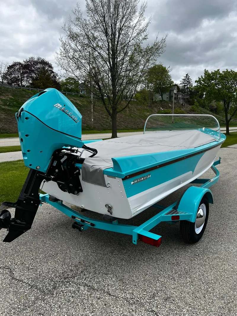 Slide: The Image of 2025 Starcraft 57 SKI CHAMP boat with turquoise and white design, parked on a street. - 3
