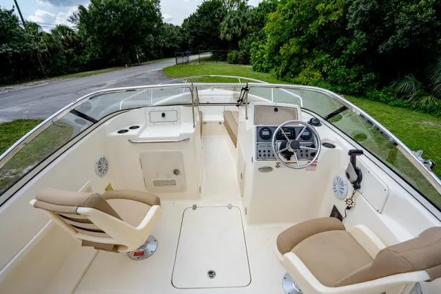 Slide: The Image of 2021 Scout 210 Dorado boat interior with dual seats and steering console, surrounded by lush greenery. - 6
