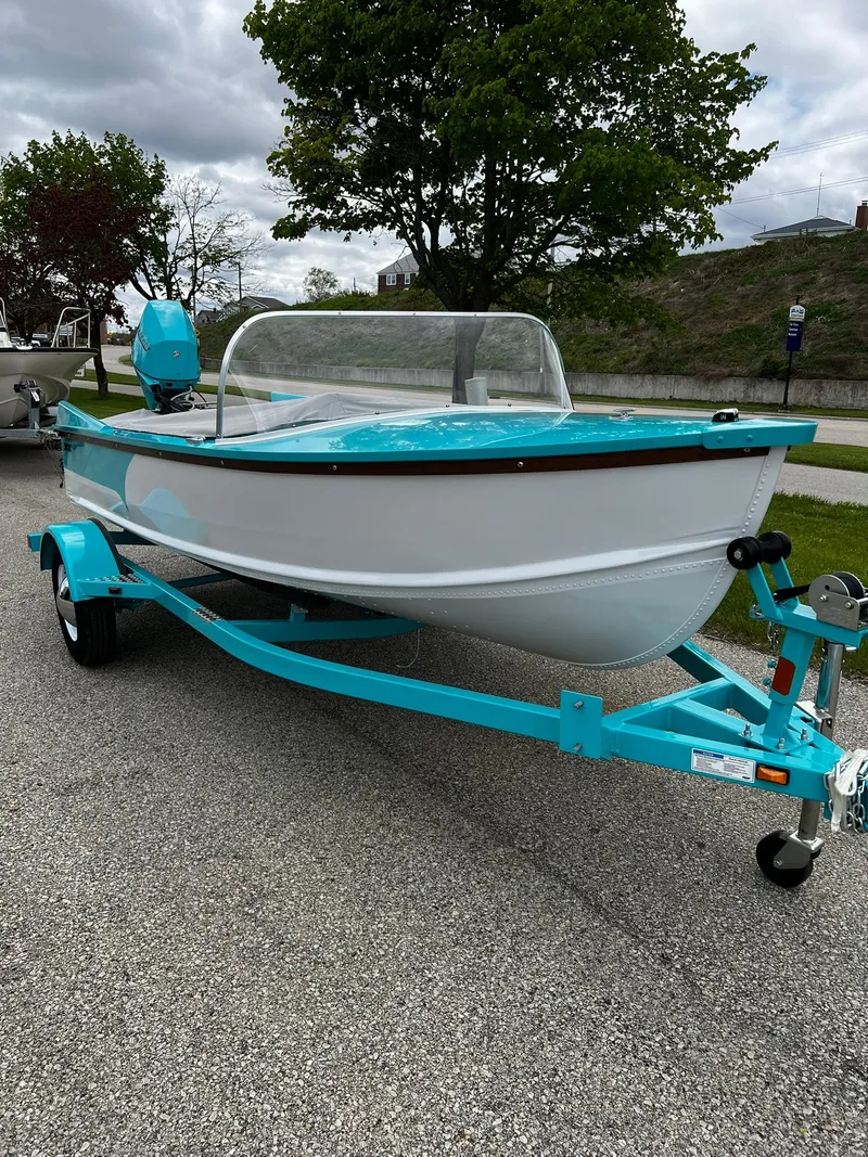 Slide: The Image of 2025 Starcraft 57 SKI CHAMP boat with turquoise accents on a trailer, parked outdoors. - 2