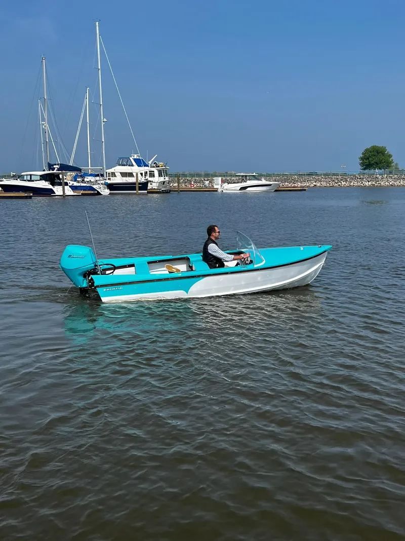 Slide: The Image of 2025 Starcraft 57 SKI CHAMP boat cruising on a calm lake with marina backdrop. - 7