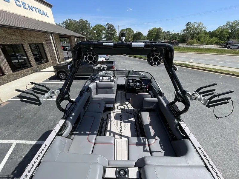 Slide: The Image of 2023 Moomba Craz boat interior with seating and wakeboard racks, parked outside a building. - 23