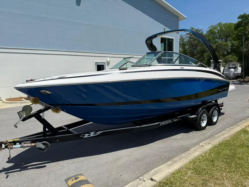 Slide: The Image of 2011 Regal 2500 Bowrider boat on trailer, blue and white, parked outdoors. - 0