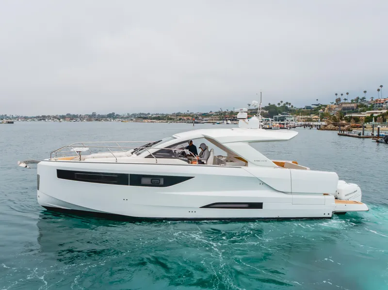 Slide: The Image of 2024 Jeanneau DB/43 OB yacht cruising on calm waters near a coastal town. - 3