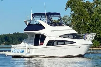 Slide: The Image of 2003 Carver 360 Sport Sedan yacht cruising on a serene lake with lush greenery. - 0