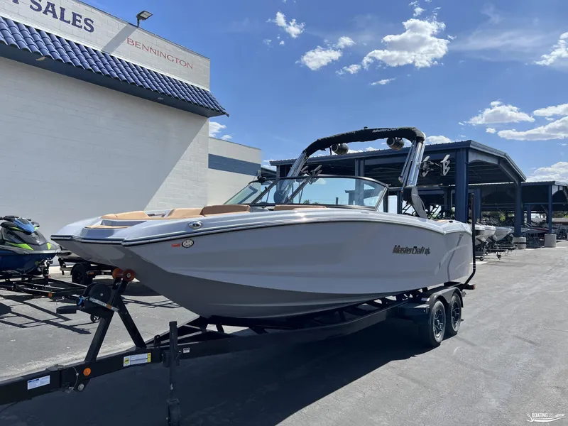 Slide: The Image of 2025 MasterCraft NXT24 boat on trailer at dealership under blue sky. - 2