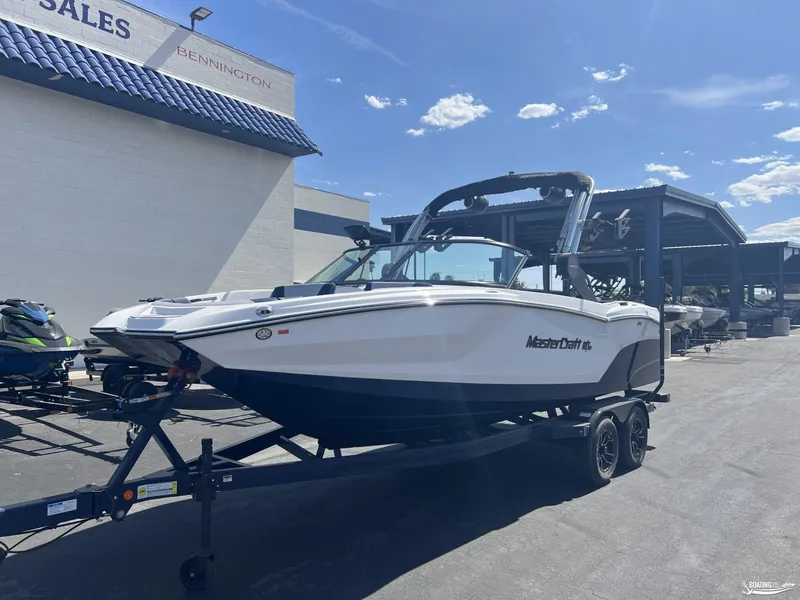Slide: The Image of 2025 MasterCraft NXT22 boat on trailer at dealership under clear blue sky. - 2