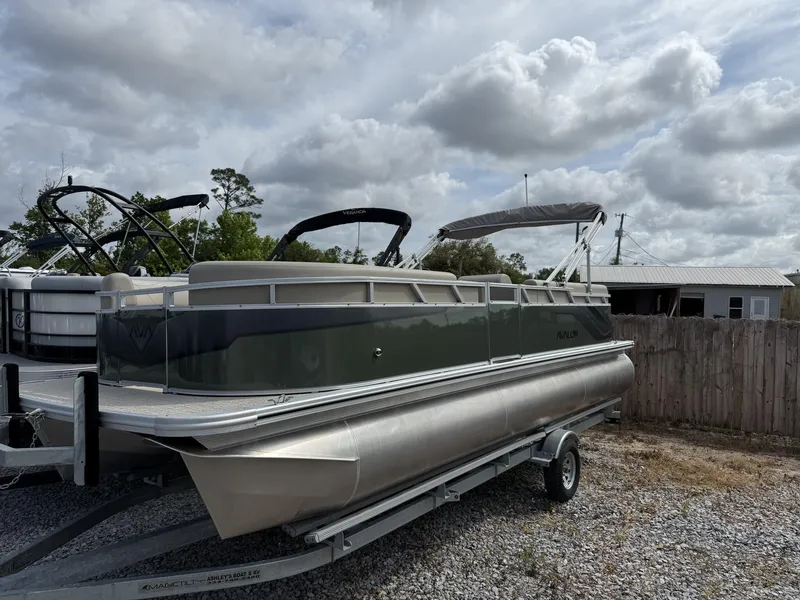 Slide: The Image of 2025 Avalon VLS 23 Quad Lounger pontoon boat on trailer, under cloudy sky. - 1