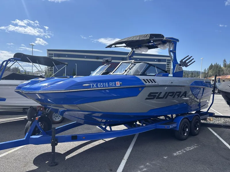 Slide: The Image of 2022 Supra SE 450 boat in blue and gray on a trailer, parked outdoors. - 2
