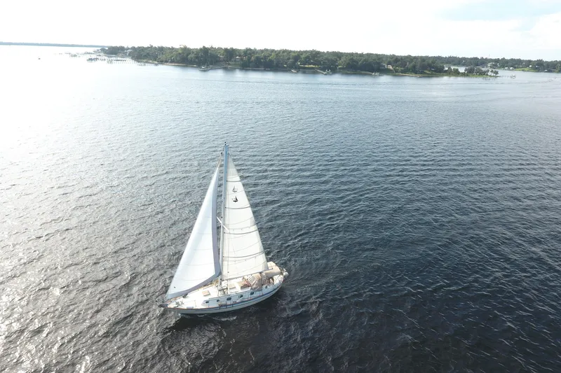 The Image of Sailboat Pacific Seacraft Crealock 37, 1986, cruising on open water near a lush shoreline. - 0