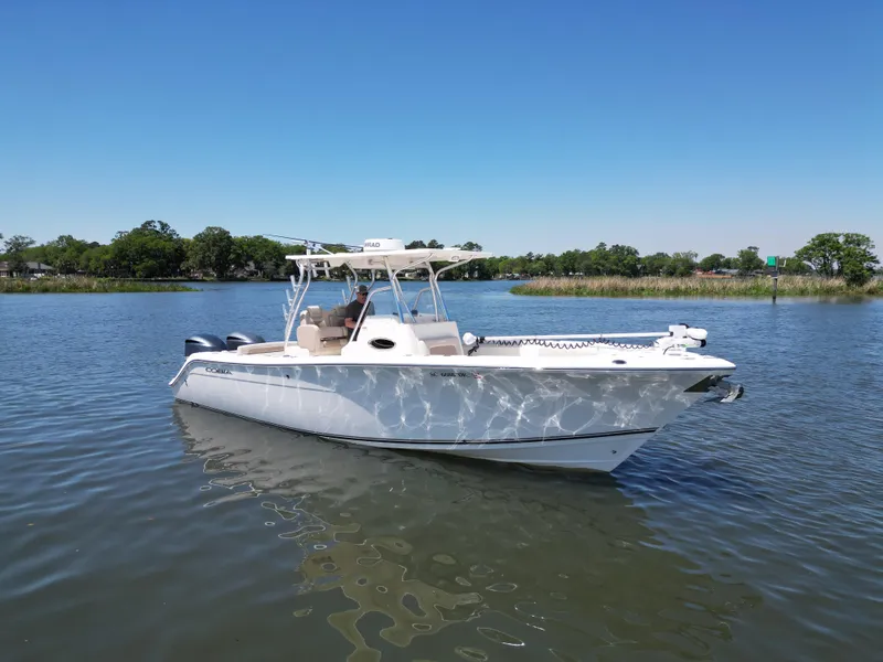 Slide: The Image of 2013 Cobia 296 Center Console boat on trailer, parked near a lake under clear blue sky. - 0