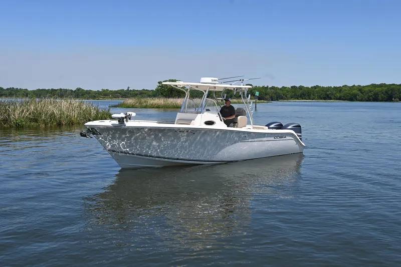 Slide: The Image of 2013 Cobia 296 Center Console boat cruising on a calm lake under clear blue skies. - 3