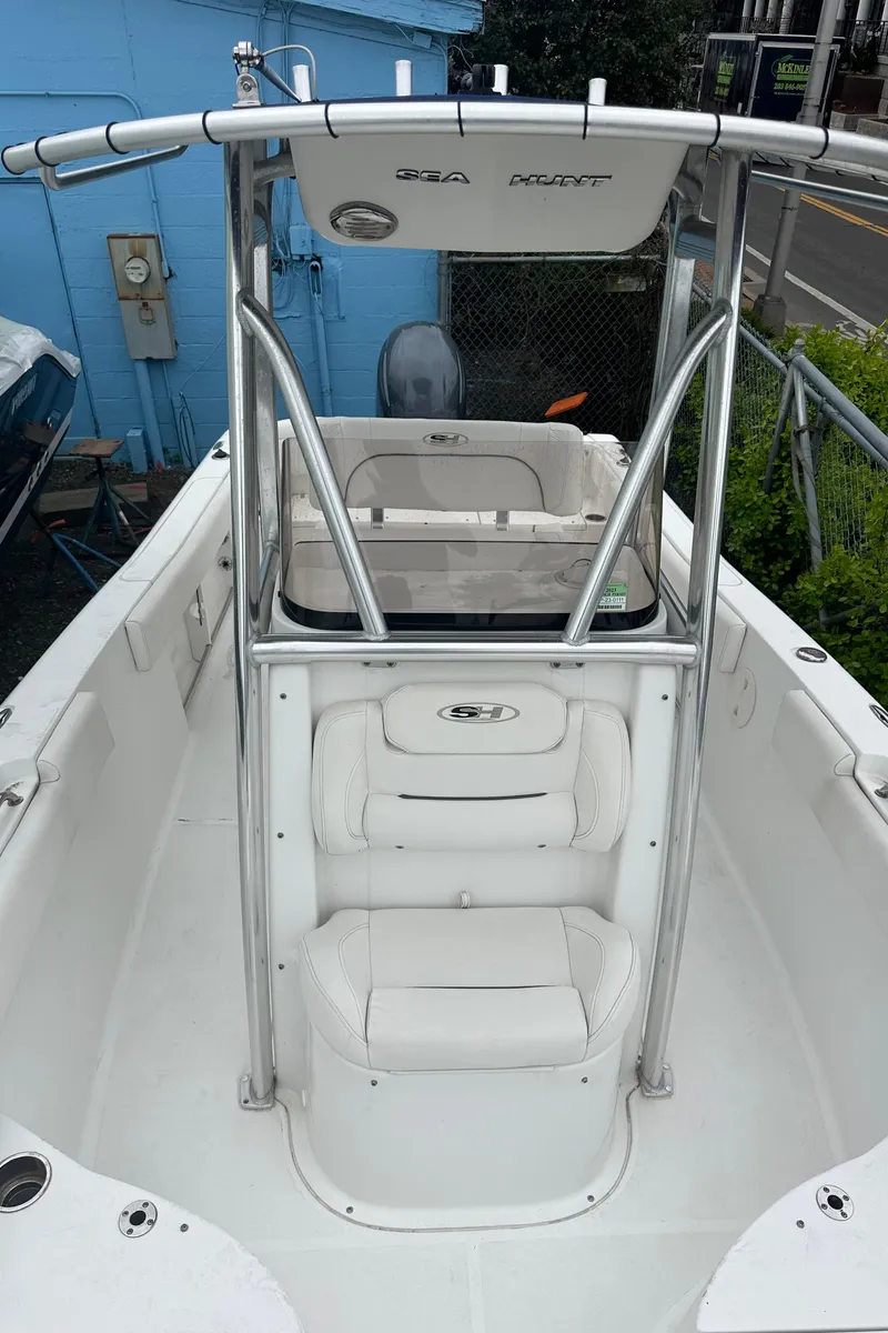 Slide: The Image of 2017 Sea Hunt Ultra 234 boat with T-top and seating, docked near a blue building. - 13