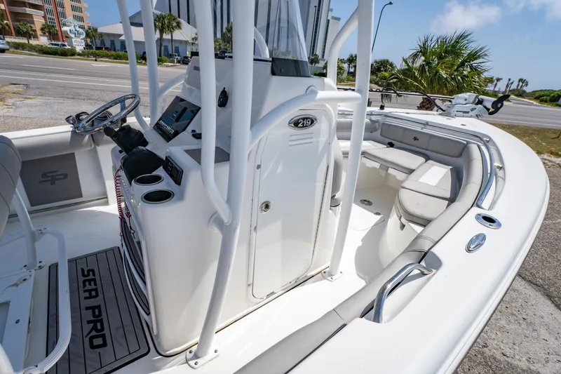Slide: The Image of 2019 Sea Pro 219 DLX boat interior with seating and console, parked near a road. - 19