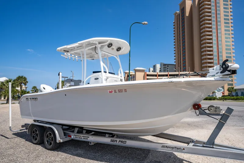 Slide: The Image of 2019 Sea Pro 219 DLX boat on trailer, parked near tall buildings under clear blue sky. - 2