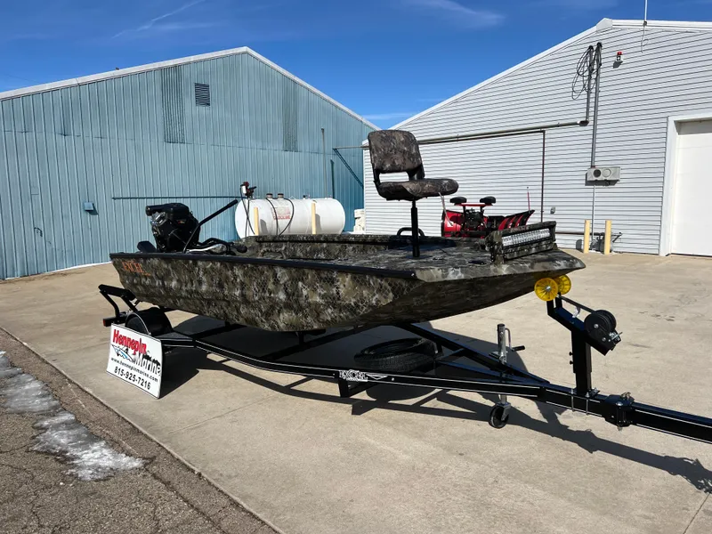 Slide: The Image of 2025 Excel Eclipse boat on trailer, camo design, parked outside industrial building. - 2