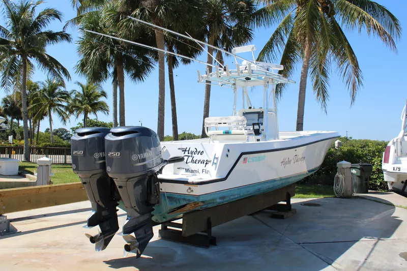 Slide: The Image of 2002 Contender 31 CC boat with dual Yamaha engines, docked under palm trees. - 13
