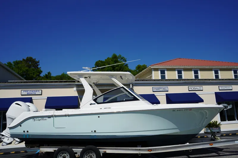 Slide: The Image of 2018 Edgewater 262 CX boat on trailer, parked in front of a building with blue awnings. - 0