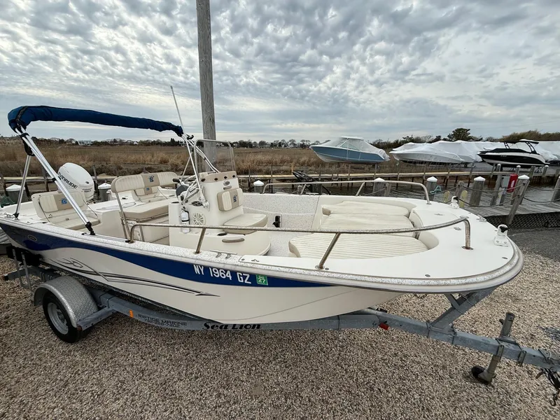 Slide: The Image of 2018 Carolina Skiff 198 DLV boat on trailer, parked near a marina under cloudy skies. - 15
