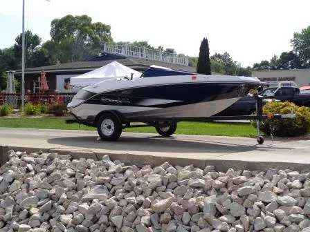 Slide: The Image of 2016 Scarab 165G boat on trailer, parked near a building with rocks in foreground. - 2