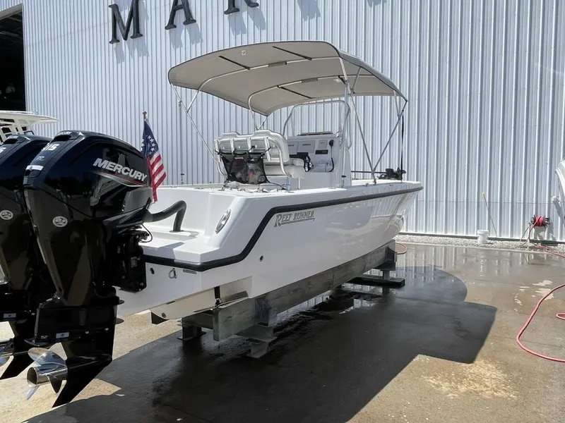 Slide: The Image of 2024 Reef Runner 230 XO boat with dual Mercury engines and canopy, docked near a marina. - 7