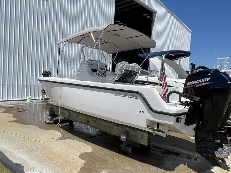 Slide: The Image of 2024 Reef Runner 230 XO boat with Mercury engine, docked near a large warehouse. - 8