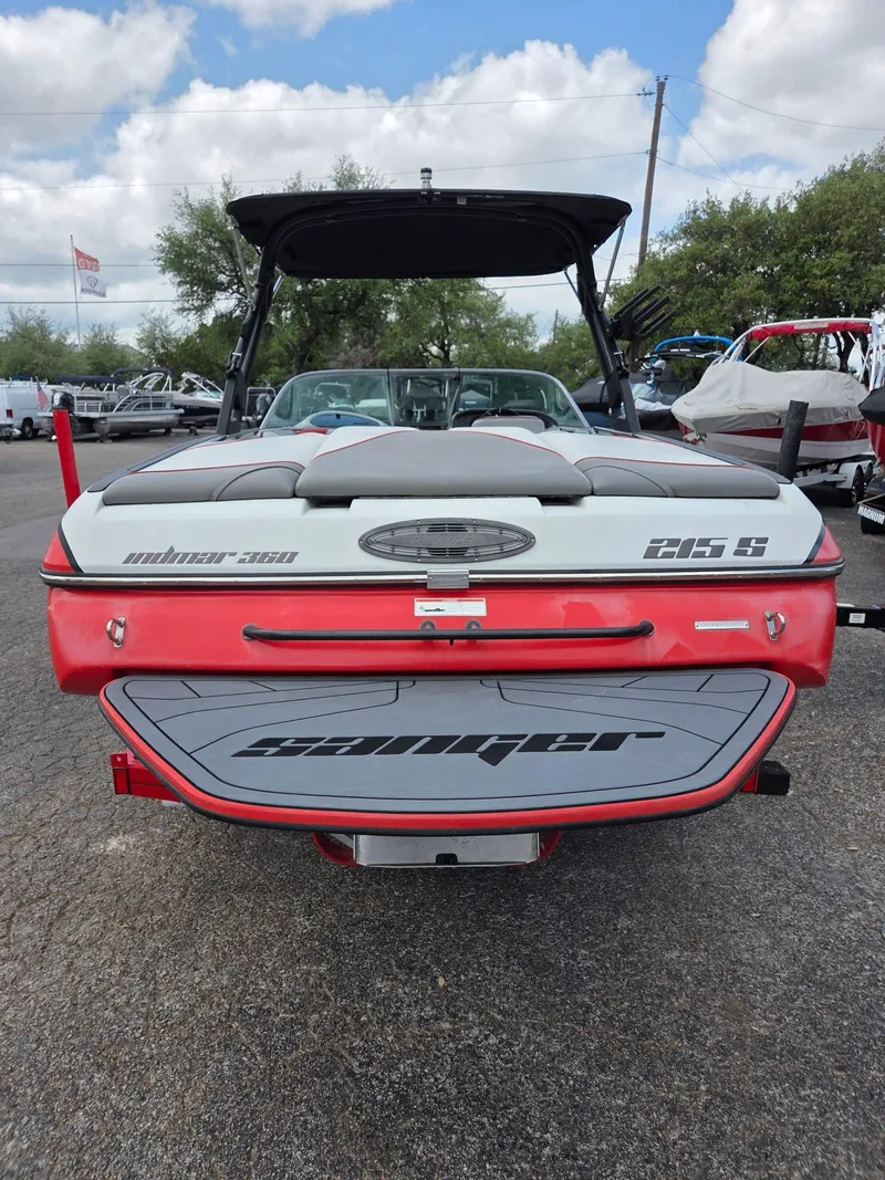 Slide: The Image of 2021 Sanger V215 S boat, red and gray, parked outdoors with a cloudy sky backdrop. - 2