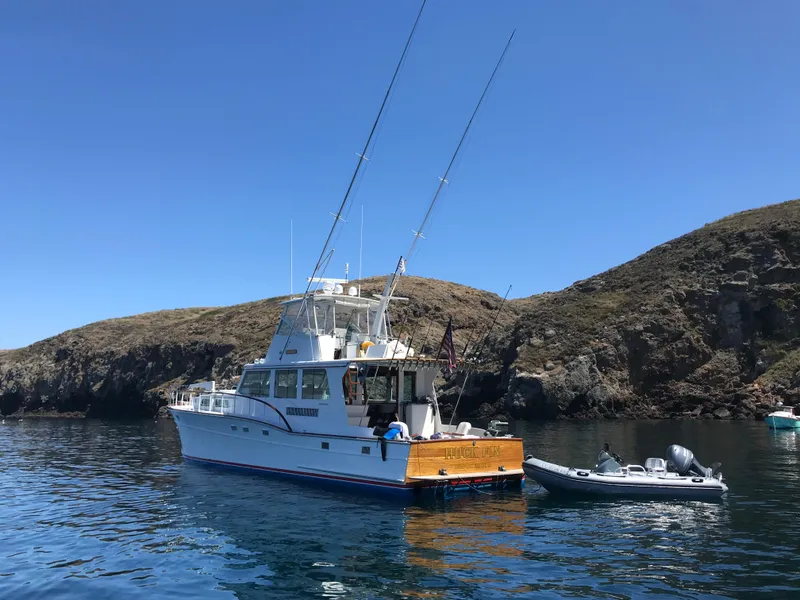 Slide: The Image of 1966 Huckins Sportsman boat anchored near rocky coastline with inflatable dinghy. - 3