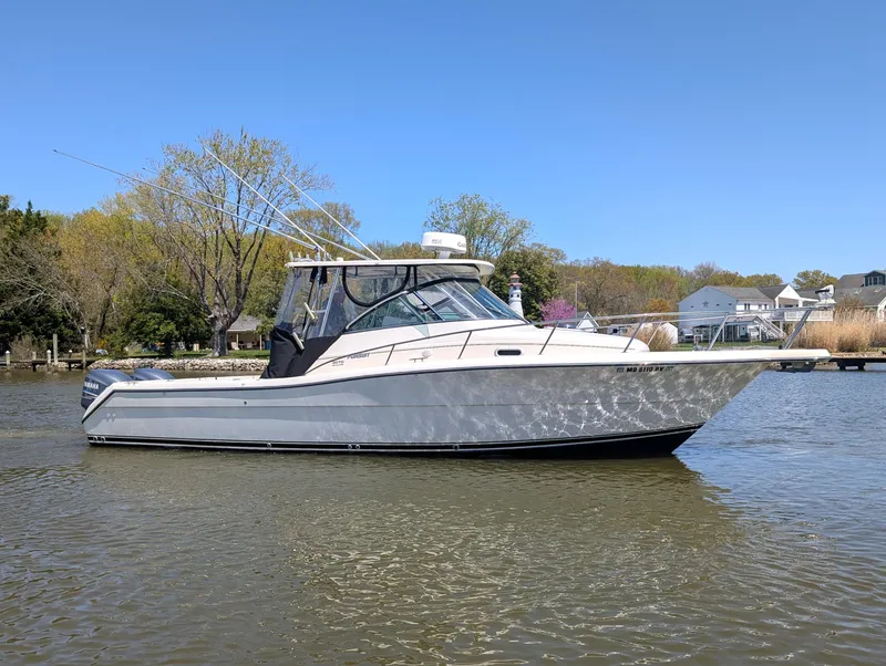 The Image of 2001 Pursuit 3070 Offshore Center Console boat on calm water, surrounded by trees and houses. - 0