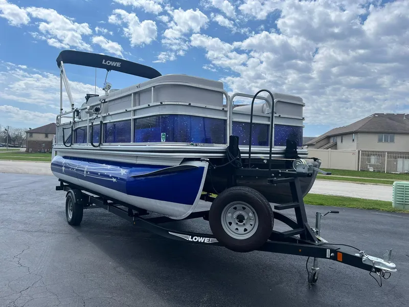 Slide: The Image of 2019 Lowe Ultra 182 Fish & Cruise pontoon boat on trailer, parked outdoors under cloudy sky. - 2