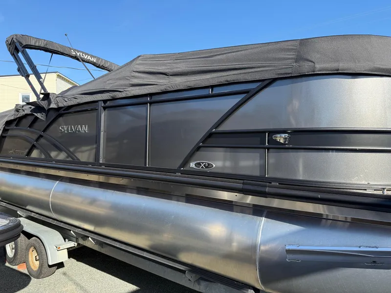 Slide: The Image of 2025 Sylvan X-3 CLZ pontoon boat with black cover on trailer. - 2