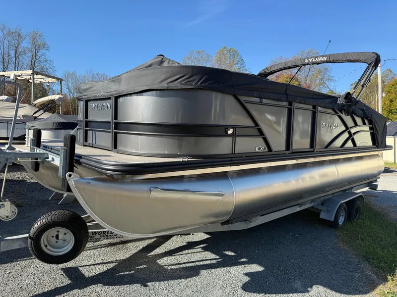 Slide: The Image of 2025 Sylvan X-3 CLZ pontoon boat on trailer, covered and parked outdoors. - 3
