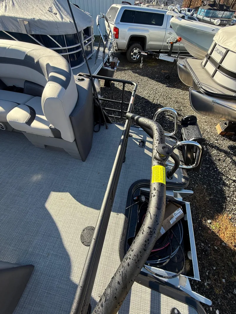 Slide: The Image of 2025 Sylvan L-3 LZ pontoon boat interior with seating and railing, parked near vehicles. - 14