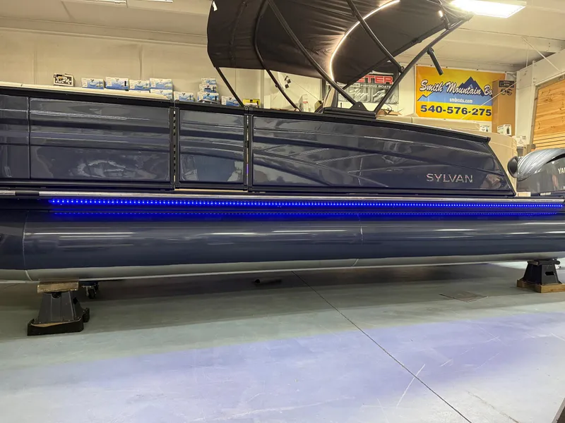 Slide: The Image of 2025 Sylvan G-3 CLZ DH pontoon boat with blue LED lights in showroom. - 2