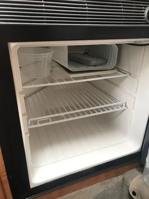 Slide: The Image of Empty mini fridge inside 2006 Sea Ray Sundancer boat, featuring wire shelves and a plastic container. - 15