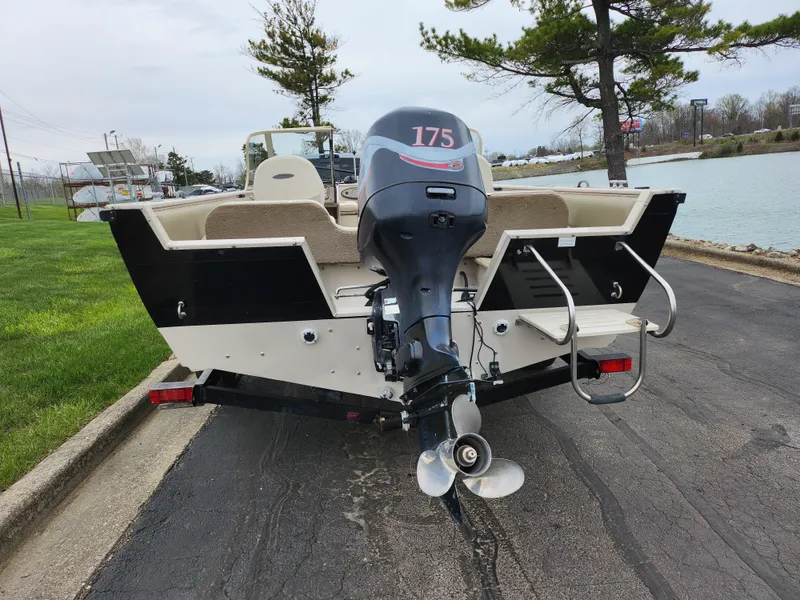 Slide: The Image of 2000 Crestliner 1850 Sportfish boat with outboard motor, parked near a lake. - 2