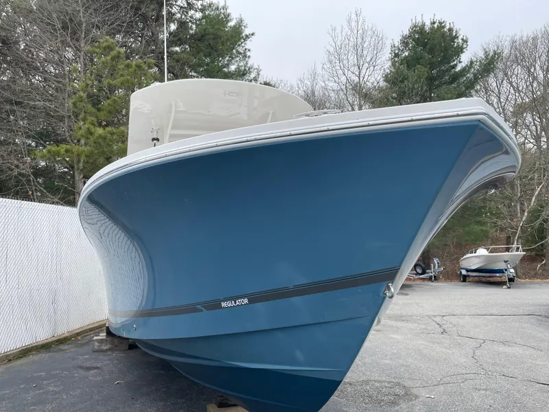 Slide: The Image of 2016 Regulator 28 boat with blue hull, parked outdoors near trees. - 1