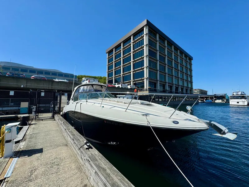 The Image of 2009 Sea Ray 350 Sundancer docked near a modern building on a sunny day. - 0