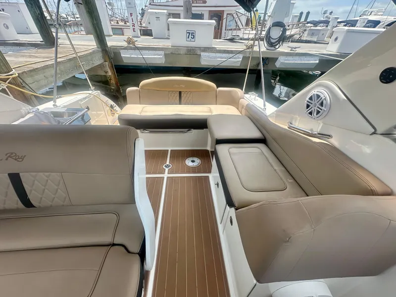 Slide: The Image of 2012 Sea Ray 310 Sundancer interior with beige seating and wood-style flooring at a marina. - 17