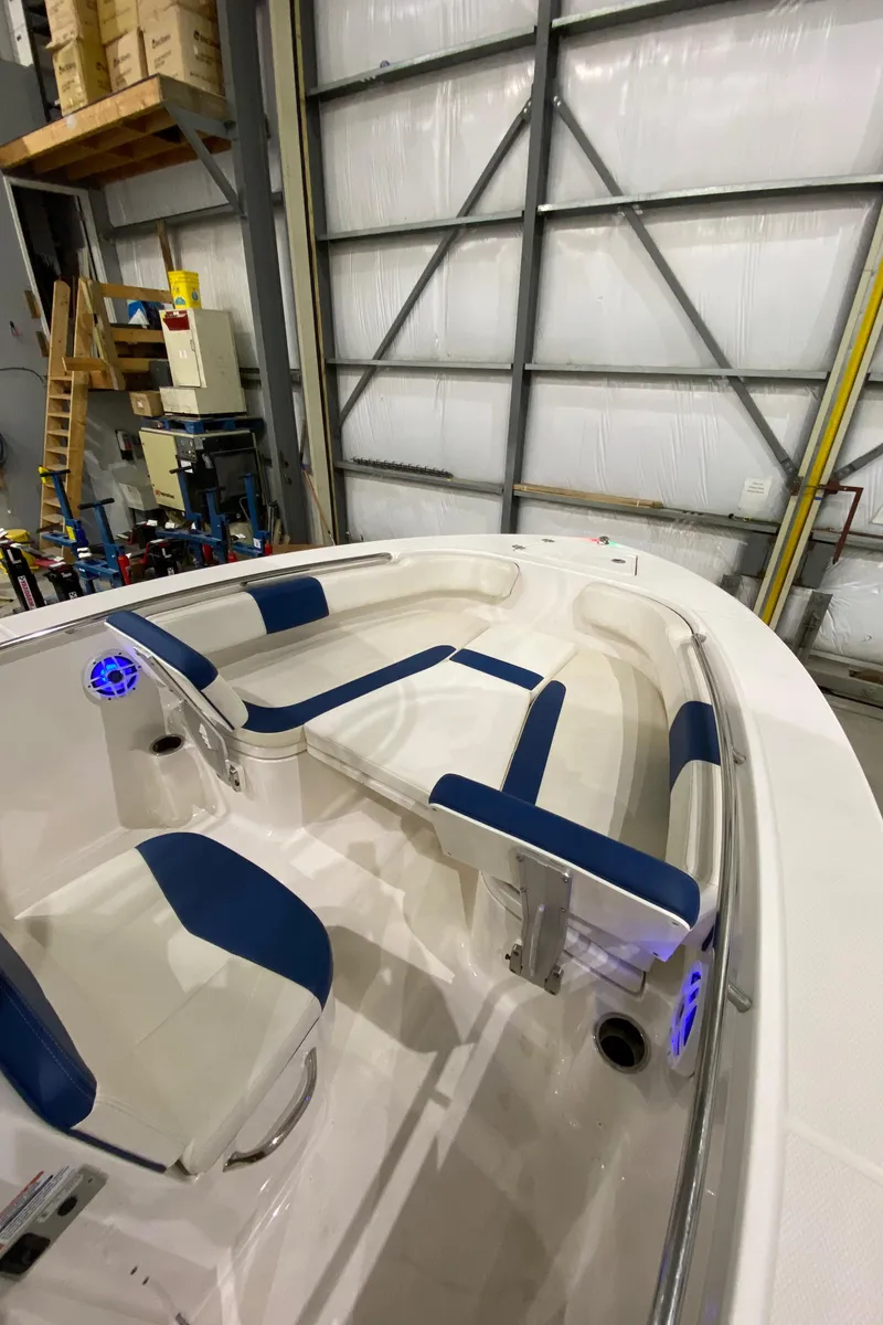 Slide: The Image of 2022 Robalo R200 Center Console boat interior with blue and white seating in a warehouse. - 19