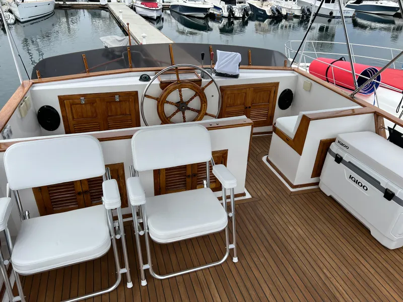 Slide: The Image of 1984 DeFever 41 Trawler helm with wooden wheel, white chairs, and docked boats in background. - 3